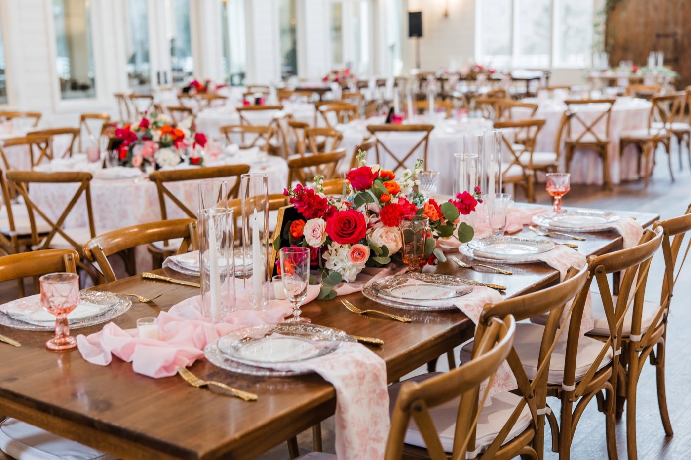 A wedding reception tablescape with pink and red florals on wooden farm tables